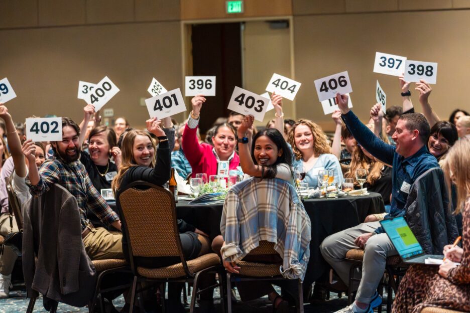 Audience members actively participating in an event, holding numbered signs while seated at tables with drinks and food, showcasing engagement and enthusiasm.